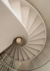 Top-down view of a pristine white spiral staircase with smooth plaster treads and a central cylindrical core, featuring clean geometric lines and soft natural lighting.
