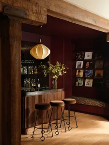 Luxurious home bar featuring a fluted walnut counter, three velvet bar stools, a large pendant lamp, and a built-in burgundy wall displaying vinyl records.