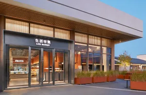 Modern retail entrance of Life Market featuring vertical wood slats, large glass doors, illuminated signage, and terracotta planters along the sidewalk.