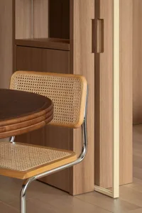 Cane and walnut dining chair with chrome frame next to a round walnut dining table in a wood-paneled dining room