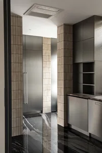 Modern minimalist kitchen corner featuring black marble flooring and walls with vertical beige tiles, stainless steel tall cabinets, and open shelving under dramatic overhead lighting.
