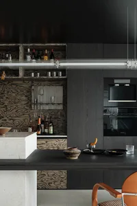 Modern dark kitchen interior with burl wood patterned cabinetry, white marble kitchen island, built-in wine bar, and black appliances under a long linear pendant light.