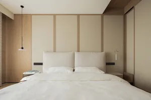 Modern minimalist bedroom featuring a large bed with a textured beige fabric headboard, white bedding, light oak wood paneling on the wall, and matching floating nightstands with pendant lights.