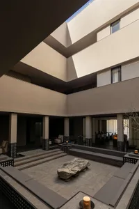 Modern sunken courtyard with built-in concrete seating, large natural boulder centerpiece, and multi-level architectural walls under an open sky.