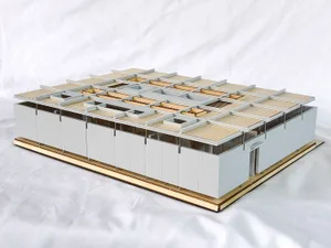 Architectural scale model of a modernist grid house with white exterior walls, natural wood roof planes, and an open interior layout, displayed on a light wood base against a white fabric background.