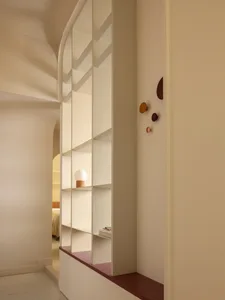 Modern arched built-in shelving unit in off-white with terracotta-colored base and decorative hooks, featuring a spherical table lamp on one shelf.