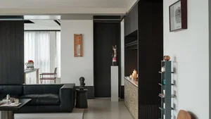 Modern monochrome living room with black leather sofa, black oak wall paneling, sculptural wooden cat figure on concrete pedestal, and built-in storage with patterned cabinet front.