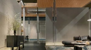 Modern minimalist living room featuring large concrete panels, warm wood slat ceiling, dark textured sofa, and sculptural floral arrangement on a black console.