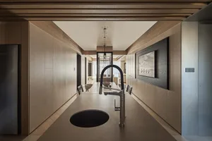 Modern minimalist kitchen with wood panel walls, concrete island, black gooseneck faucet, and framed artwork in a long corridor layout.