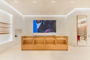 Modern minimalist retail store interior with white walls, glossy floor, recessed lighting, and a central light oak display counter with glass top.