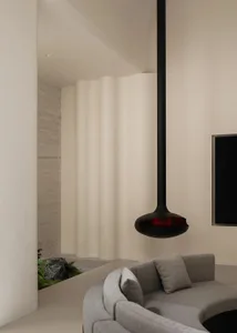 Modern living room featuring a curved grey fabric sofa, a large black sculptural pendant lamp, a textured travertine wall, and an indoor rock garden with moss and ferns.