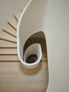 Top-down view of a modern spiral staircase featuring a smooth white curved balustrade and light-colored oak wooden steps set against a neutral-toned interior.