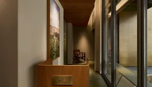 Narrow modern hallway featuring a curved oak reception desk, large landscape photograph, wooden chair, and warm ambient lighting.
