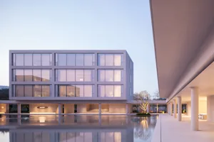 Modern minimalist concrete house with large reflecting pool at dusk, showing symmetrical grid windows and covered walkway with columns.