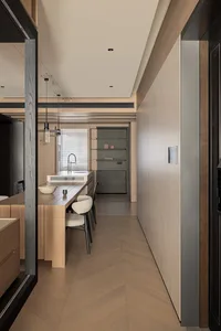 Modern minimalist kitchen featuring a light oak island with integrated sink, two boucle upholstered bar stools, herringbone wood flooring, and built-in grey cabinetry at the far end.