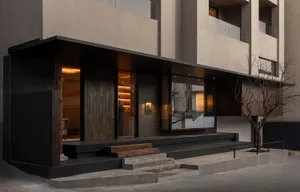 Modern building entrance with dark wood panels, large glass windows, concrete steps, and a leafless tree at dusk