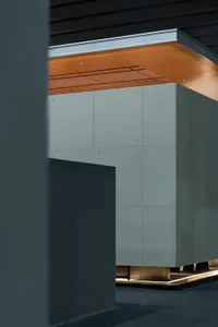 Modern architectural interior featuring a large floating concrete cabinet with visible bolt details, warm wood ceiling with linear slats, and dramatic indirect lighting at the base.
