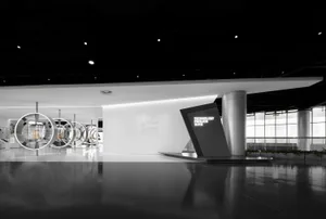 Spacious modern exhibition hall with polished concrete floors, white walls, circular metallic display structures, and a black Technology Pavilion sign under dramatic ceiling lighting.