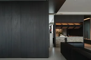 Modern minimalist living room interior featuring dark walnut wood paneling, black leather sofa, and a marble console with sculptural objects.