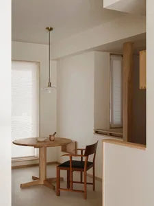 極簡用餐角落，包含圓形橡木餐桌、黑色座面的木製扶手椅，以及懸掛上方的白色 PH 風格吊燈。