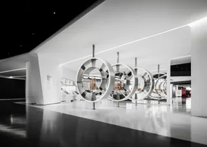 Large circular stainless steel sculptures displayed in a spacious, modern white exhibition hall with polished floors and linear lighting.
