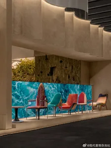 Modern lounge area featuring a curved textured plaster staircase, a large turquoise ocean wave mural, and a row of colorful mid-century modern lounge chairs in teal, red, pink, and orange.