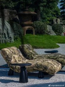 Two sculptural chaise lounges with stone-like texture placed on white gravel in a traditional Japanese garden featuring a stone lantern, rocks, and manicured greenery.