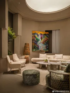 Modern curved living room featuring a creamy white curved sofa, travertine coffee tables, a green fur ottoman, and a large colorful abstract landscape painting on a curved beige wall.