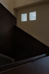 Close-up view of a dark oak wooden staircase with thick handrail and paneling, featuring two square recessed light niches in the upper beige wall.