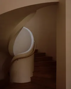 View of a modern curved staircase featuring a smooth white plaster balustrade, warm wooden handrail, and dark walnut treads ascending into soft beige walls.