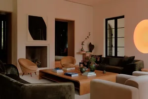 Modern living room featuring dark green velvet sofas, tan curved armchairs, a large oak coffee table, minimalist fireplace, and large spherical wall light.