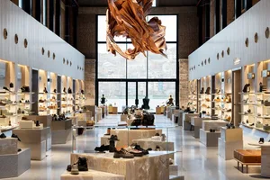 Modern shoe store interior with white marble display platforms, recessed wall shelving, polished concrete floor, and a large abstract copper chandelier hanging in the center.