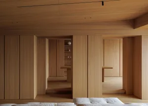 Modern minimalist living room interior featuring extensive light oak wood cabinetry, built-in shelving, and a white fabric sofa in the foreground.
