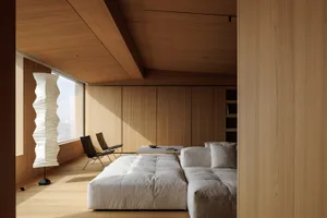 Modern minimalist living room featuring a large low-profile light gray sectional sofa, wooden ceiling and wall paneling, a tall white Akari-style paper floor lamp, and two black leather lounge chairs by the window.