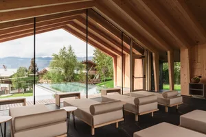 Modern wooden living room with low beige sofas, large glass walls opening to an infinity pool and mountain landscape