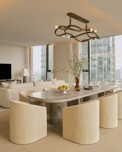 Modern luxury dining area featuring a large Calacatta marble table, six cream bouclé curved chairs, and an artistic bronze chandelier with floor-to-ceiling city views in the background.