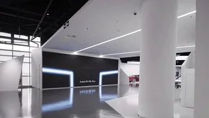 極簡白色汽車展示間，大型黑色牆面搭配發光藍色霓虹矩形光框，高反射磨光地板、白色圓柱，以及背景展示的 Lancia 汽車。