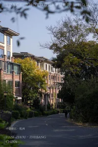 Tree-lined pathway through a modern residential community featuring brick and stucco townhouses in Hangzhou, Zhejiang, China during autumn.