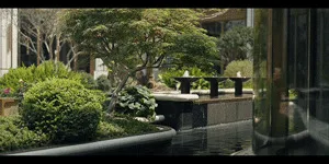 Traditional Japanese courtyard garden with a black stone tsukubai water basin, pruned shrubs, pine trees, and a shallow reflecting pool.