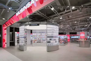 Modern beauty store interior with a large circular fragrance kiosk made of translucent acrylic shelves and integrated lighting, under a pink digital banner reading MUSINSARA.