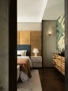 View into a modern luxury bedroom showcasing a deep teal upholstered bed against a gold leaf paneled headboard wall, a marble nightstand with grid lamp, dark wood flooring, and a teal crane-pattern wallpaper on the right wall.