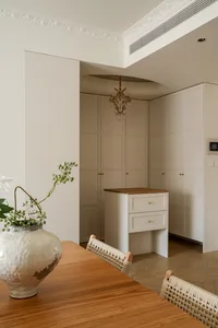 Elegant dining area featuring a wooden console table, woven rattan dining chairs, a large ceramic vase with greenery, and tall cream-colored built-in cabinetry with crown molding.