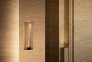 Close-up of a luxurious travertine wall featuring a recessed illuminated niche displaying a white abstract sculpture on a black base.