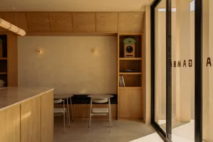 Modern minimalist dining area featuring light oak cabinetry, built-in upholstered bench, round tables with metal chairs, and a tall shelving unit displaying a speaker and vinyl records.