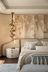 Elegant modern luxury bedroom with a large Chinese-style folding screen painted with wisteria flowers, a sculptural brass and crystal chandelier, curved upholstered bed with blue and cream pillows, round white nightstand, and light blue patterned rug.