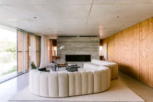 Modern living room featuring a large curved boucle sofa, concrete walls, vertical wood paneling, and a black woven accent chair in front of a fireplace.