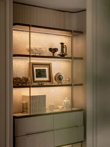 Elegant built-in shelving unit with brass frame, backlit textured glass panels, and decorative objects including books, framed art, and ceramic pieces.