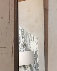 Close-up of a modern bathroom vanity mirror with white and green marble panel, stainless steel accessories, and raw concrete wall surround.