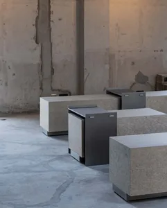 Modular concrete and metal cube furniture arranged in an empty industrial loft with raw concrete walls and polished floor.