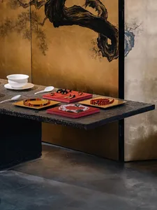 深色石材玄關桌上，以紅色與金色托盤展示色彩豐富的珠寶，背景為奢華金箔屏風，繪有傳統水墨山水畫。